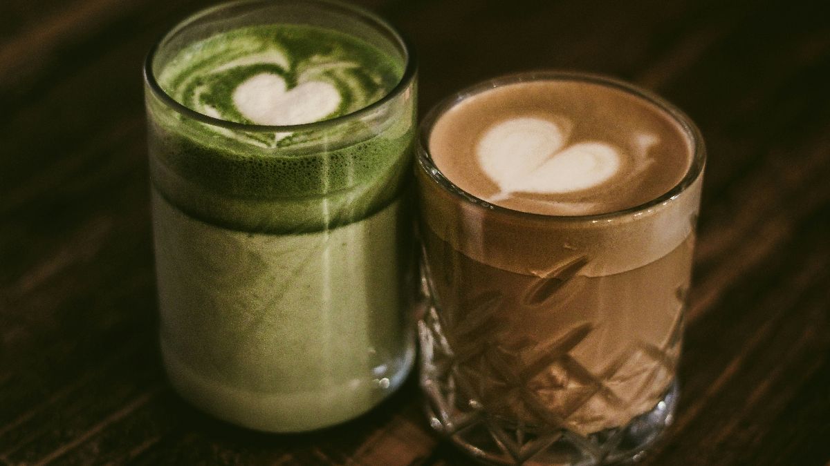 Zwei Heißgetränke im Vergleich: grüner Matcha Latte und Kaffee auf einem dunklen Holztisch