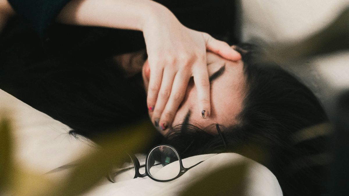 Erschöpfte Frau liegt auf dem Sofa mit Hand über dem Gesicht – symbolisch für chronische Müdigkeit als mögliches Signal eines gestörten Darm-Mikrobioms