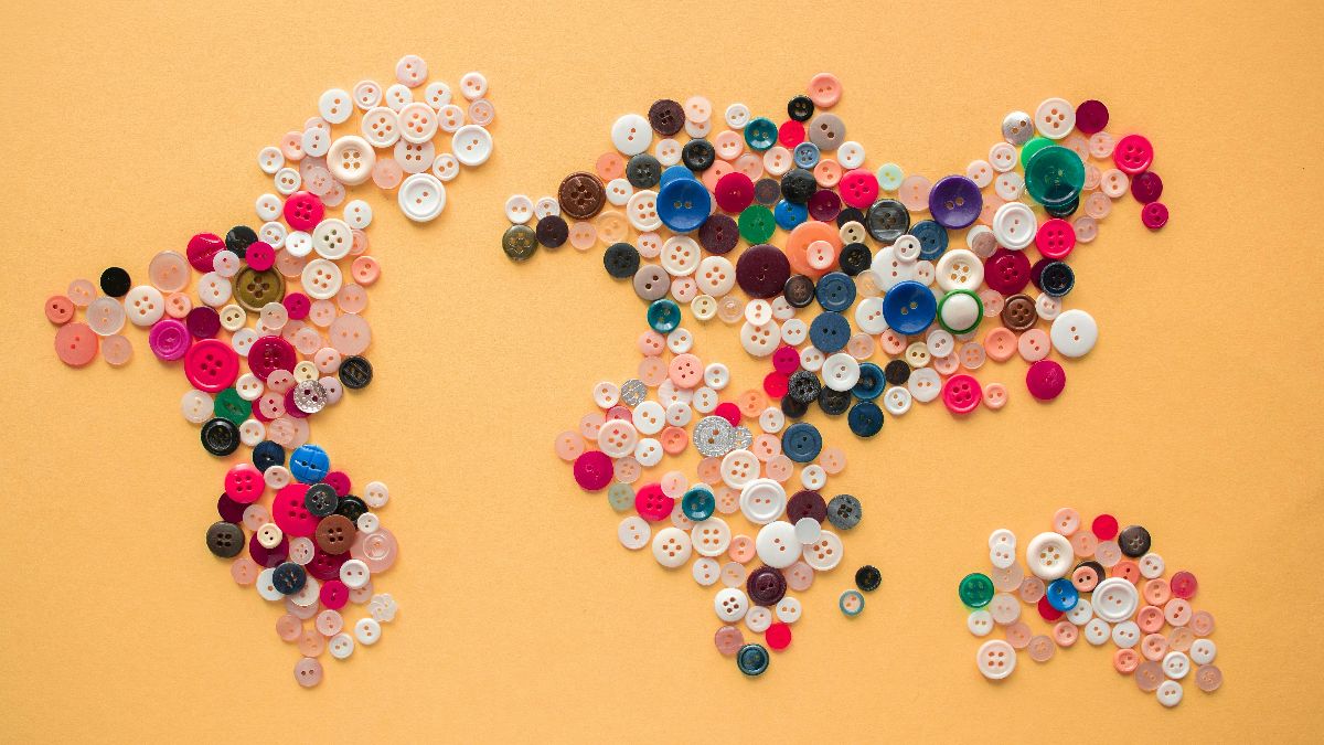 Weltkarte aus bunten Knöpfen auf gelbem Hintergrund – symbolisch für die globale Fruchtbarkeitskrise und sinkende Geburtenraten weltweit