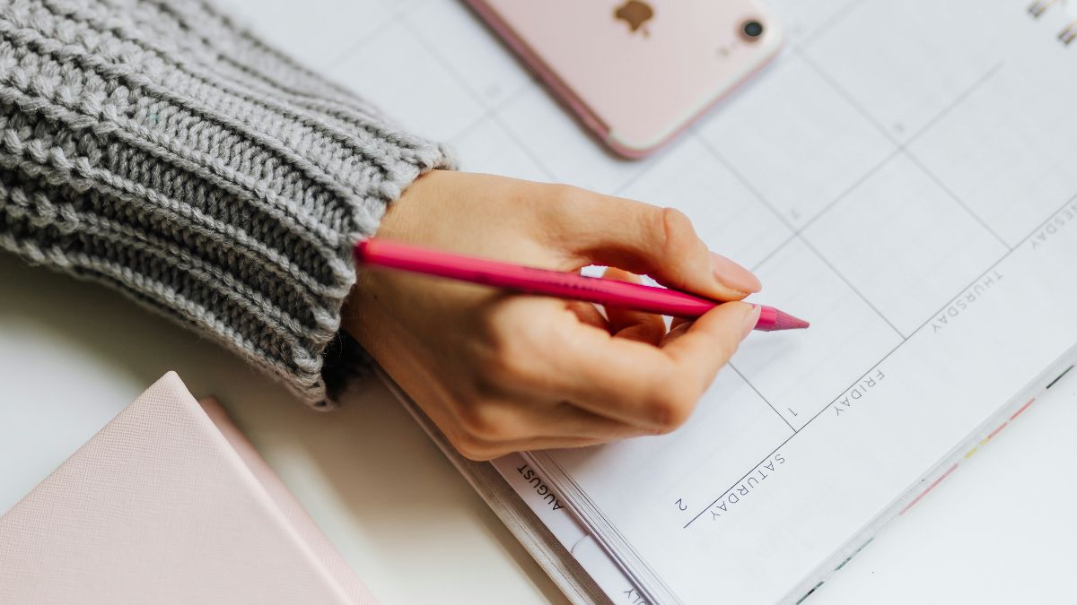 Frau trägt Zyklustage in einen Kalender ein, neben ihr liegt ein Smartphone.