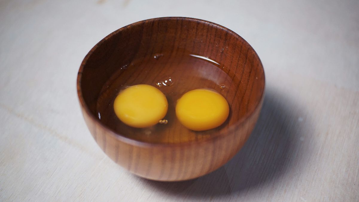 Zwei Eigelb in einer Holzschüssel – Symbol für den doppelten Eisprung und die genetische Veranlagung zu zweieiigen Zwillingen beim Kinderwunsch